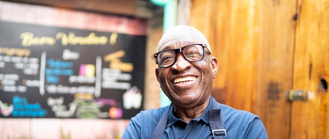 Man wearing apron standing outside business smiling.