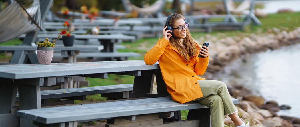 Woman using phone sitting at a picnic table by a lake.