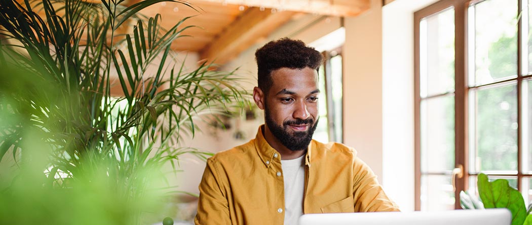 Man using laptop in well-lit room with plants.