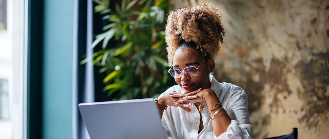 Woman looking at laptop in room with windows and plants.