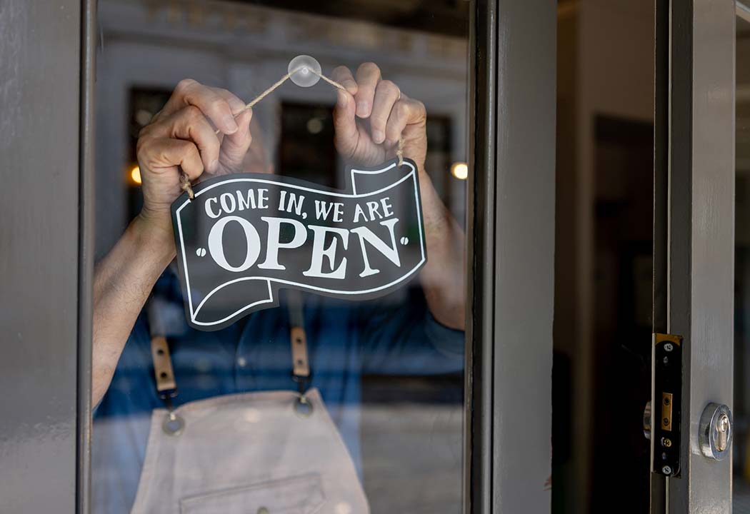 Man putting up Come in, we are open sign.